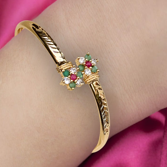 Gold bracelet with gemstone accents on a wrist against a pink background