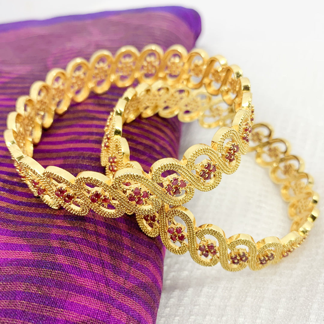 Bridal-style gold-plated bangles with detailed infinity pattern and vibrant ruby accents – traditional jewelry for special occasions