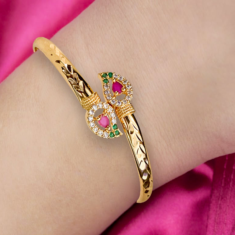 Gold bracelet with gemstones on a wrist against a pink background