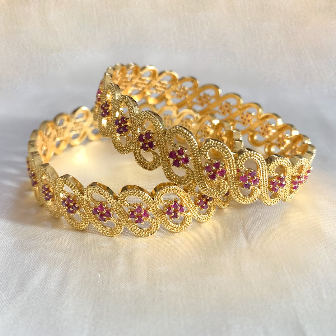 Gold-plated bangles with ruby-colored stones and intricate infinity design – elegant bridal and festive jewelry for women