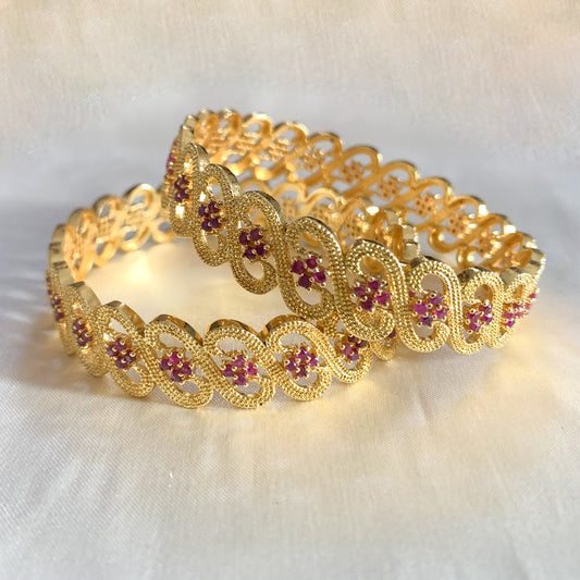 Gold-plated bangles with ruby-colored stones and intricate infinity design – elegant bridal and festive jewelry for women