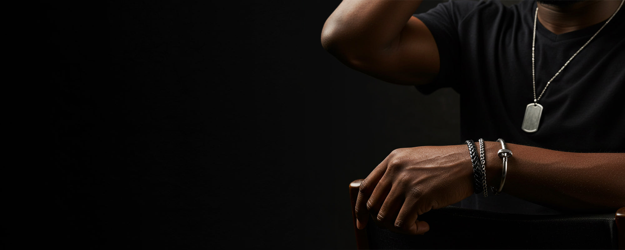 Person wearing a black shirt and multiple bracelets on a dark background