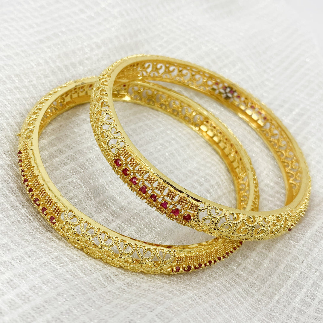Traditional gold-toned bangles with intricate filigree work and pink stones – elegant accessory for cultural celebrations